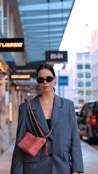 Elegant woman in sunglasses walking on city sidewalk with stylish attire.