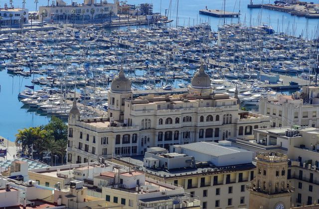 Aerial view of Alicante marina with boats and historic architecture under a clear blue sky. — arriving in Alicante