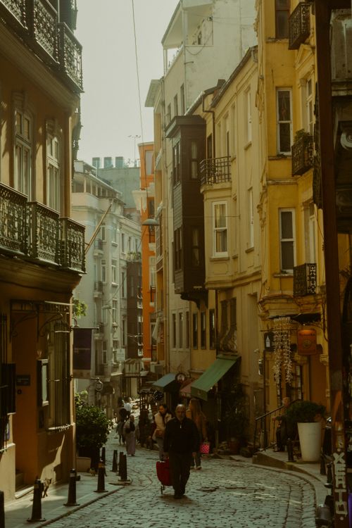 Free A narrow, lively street in Istanbul with classic architecture and people strolling under the warm sunlight. Stock Photo