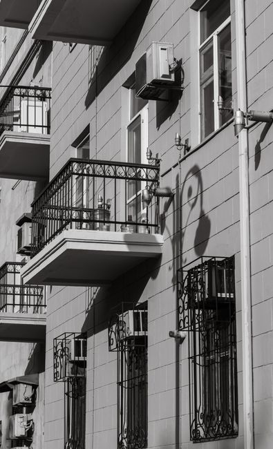 Black and white photo of a residential building facade with balconies and shadows creating urban depth.