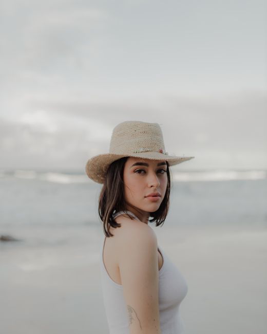 A young woman in a sun hat gazes over her shoulder at a beach on the Gold Coast, Australia.