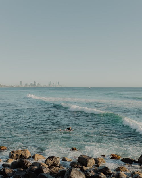 Photo of a Surfer in a Bay with a City Coastline in the Background