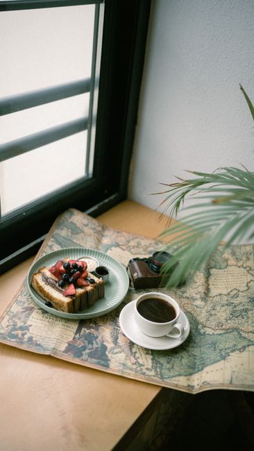 Charming breakfast setup with coffee, pastries on vintage map, perfect for travel inspiration.