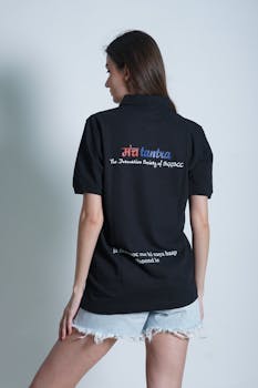 Back view of a woman in casual fashion with a black t-shirt and denim shorts standing against a white background.