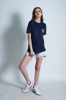 Woman posing casually in a studio wearing denim shorts and a navy t-shirt, exuding summer style.