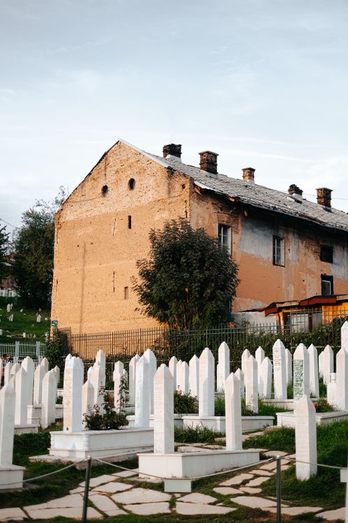 Free A serene view of a historic cemetery with traditional white tombstones and an old building backdrop. Stock Photo
