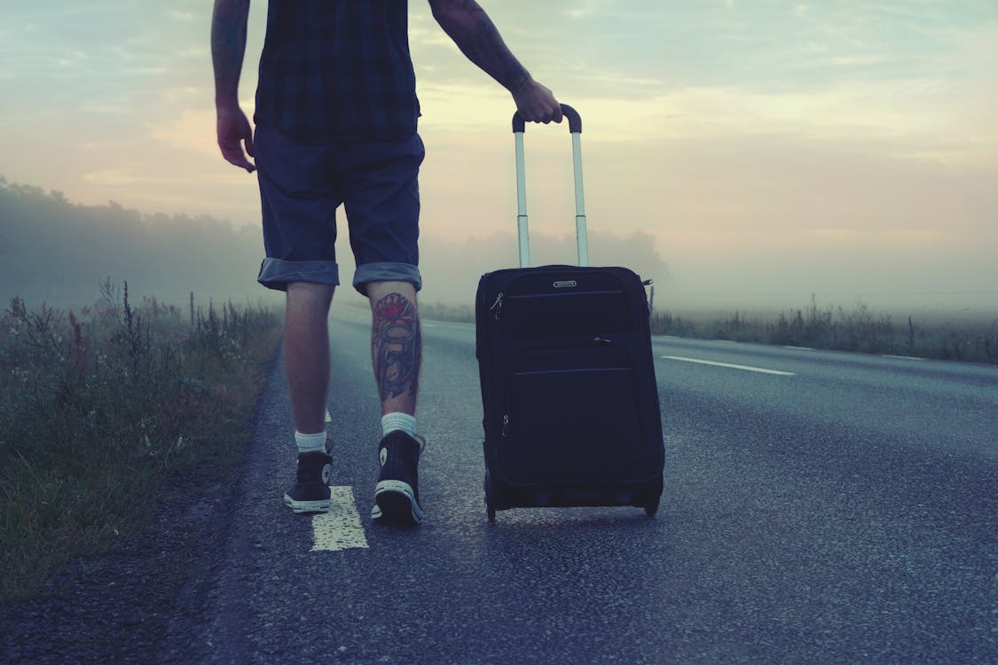 Free Man Walking on the Road Holding Black Luggage during Sunset Stock Photo