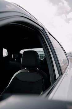 View into a car's interior through an open window, showcasing the seat and cloudy sky.
