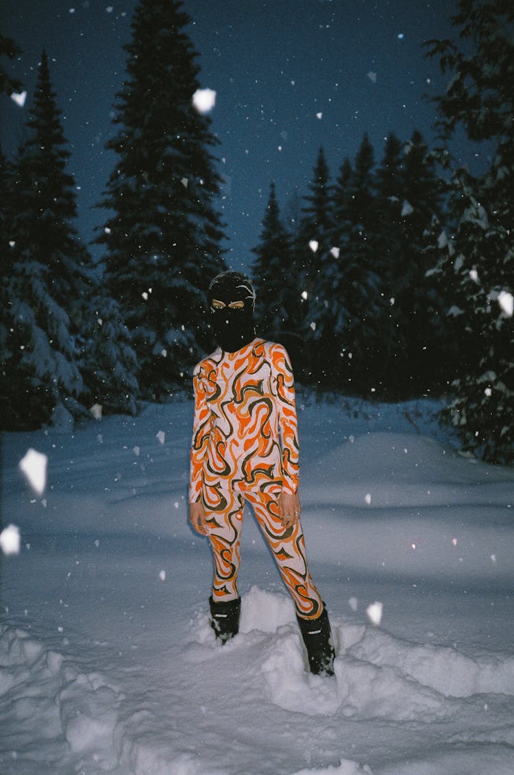 Person In Colorful Outfit And Black Balaclava In A Winter Forest At Night