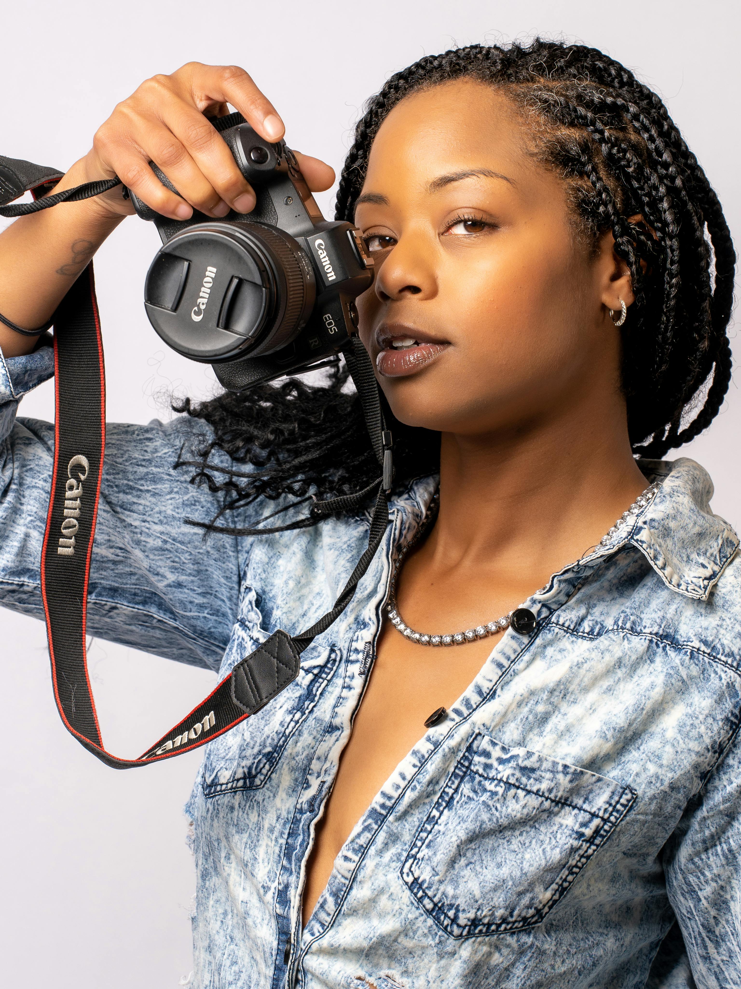 Confident woman with braided hair holding a camera in a studio setting.