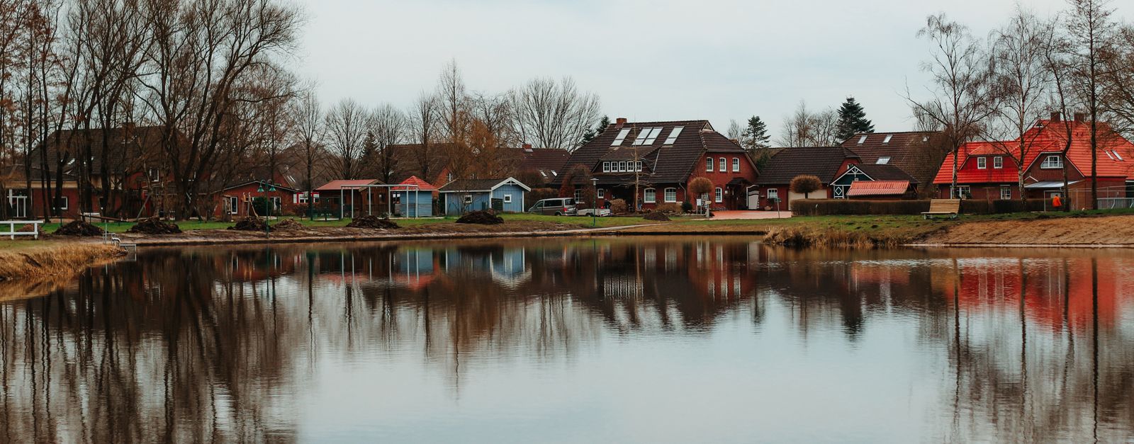 Charming lakeside houses reflecting in a serene autumn lake in Aurich, Germany.