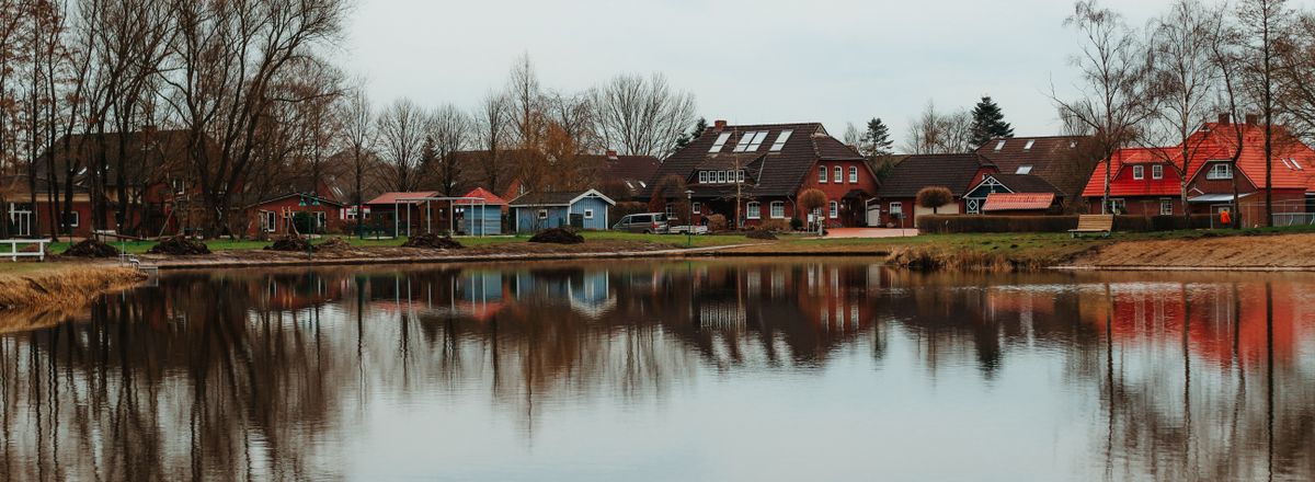 Charming lakeside houses reflecting in a serene autumn lake in Aurich, Germany.