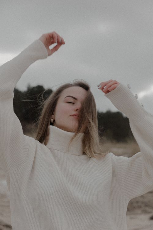Free Young woman in a white sweater enjoying a serene moment outdoors with a natural backdrop. Stock Photo