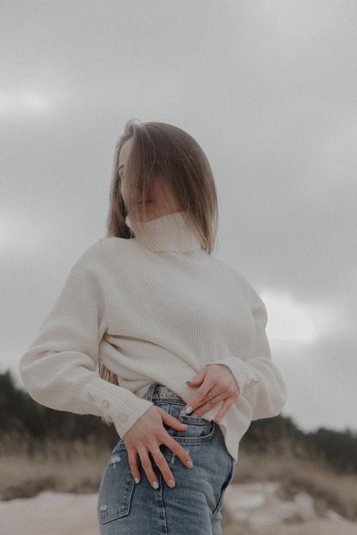 Free Stylish woman posing outdoors in a cozy winter sweater and jeans, exuding calm and elegance. Stock Photo
