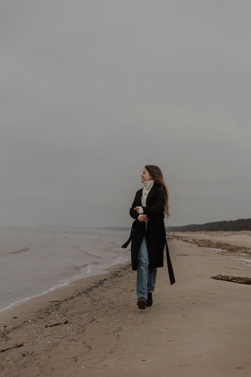 Free Long-haired woman walking on a quiet beach during winter. Calm sea and sandy shore. Stock Photo