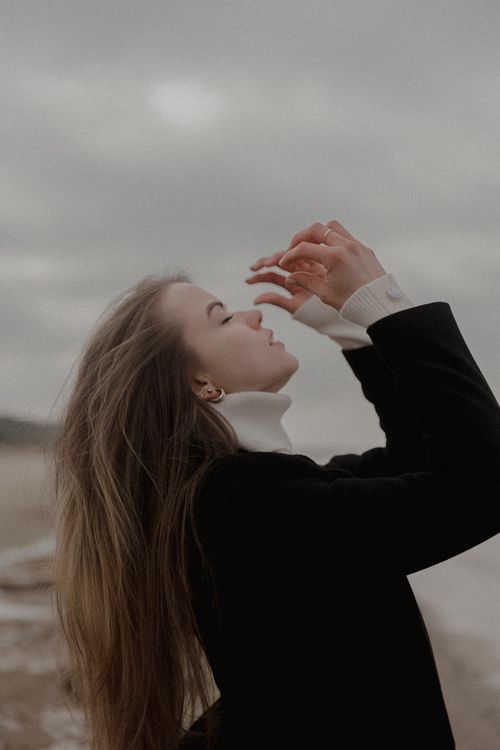 Free A woman enjoys a serene moment by the beach, capturing elegance and tranquility. Stock Photo