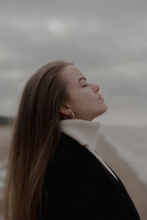 Free A woman stands peacefully on a beach, embracing the serene winter atmosphere. Stock Photo