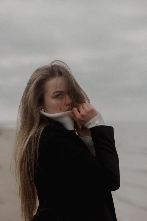 Free A woman with long hair stands pensively at a beach, wrapped in warm clothing. Stock Photo
