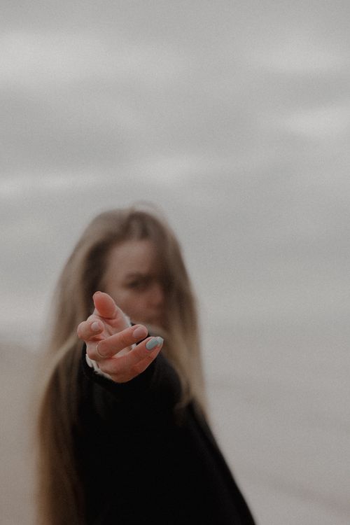 Free Blurred portrait of a woman reaching out with focus on her hand on a cloudy beach. Stock Photo