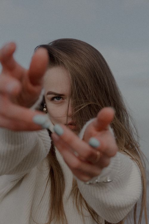 Free Artistic portrait of a woman in a sweater reaching towards the camera outdoors. Stock Photo