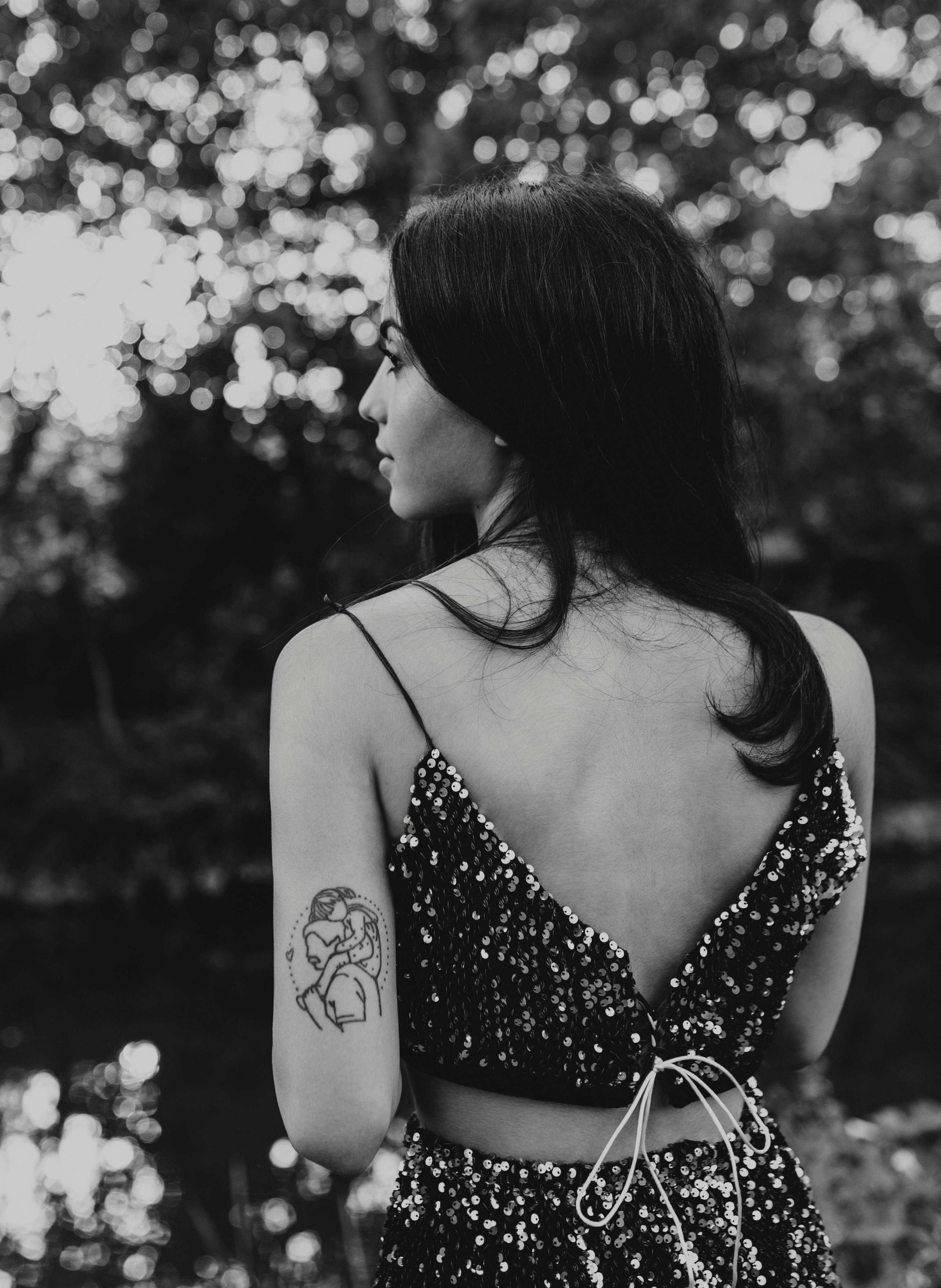 Black and white photo of a stylish woman with a back tattoo outdoors in summer.