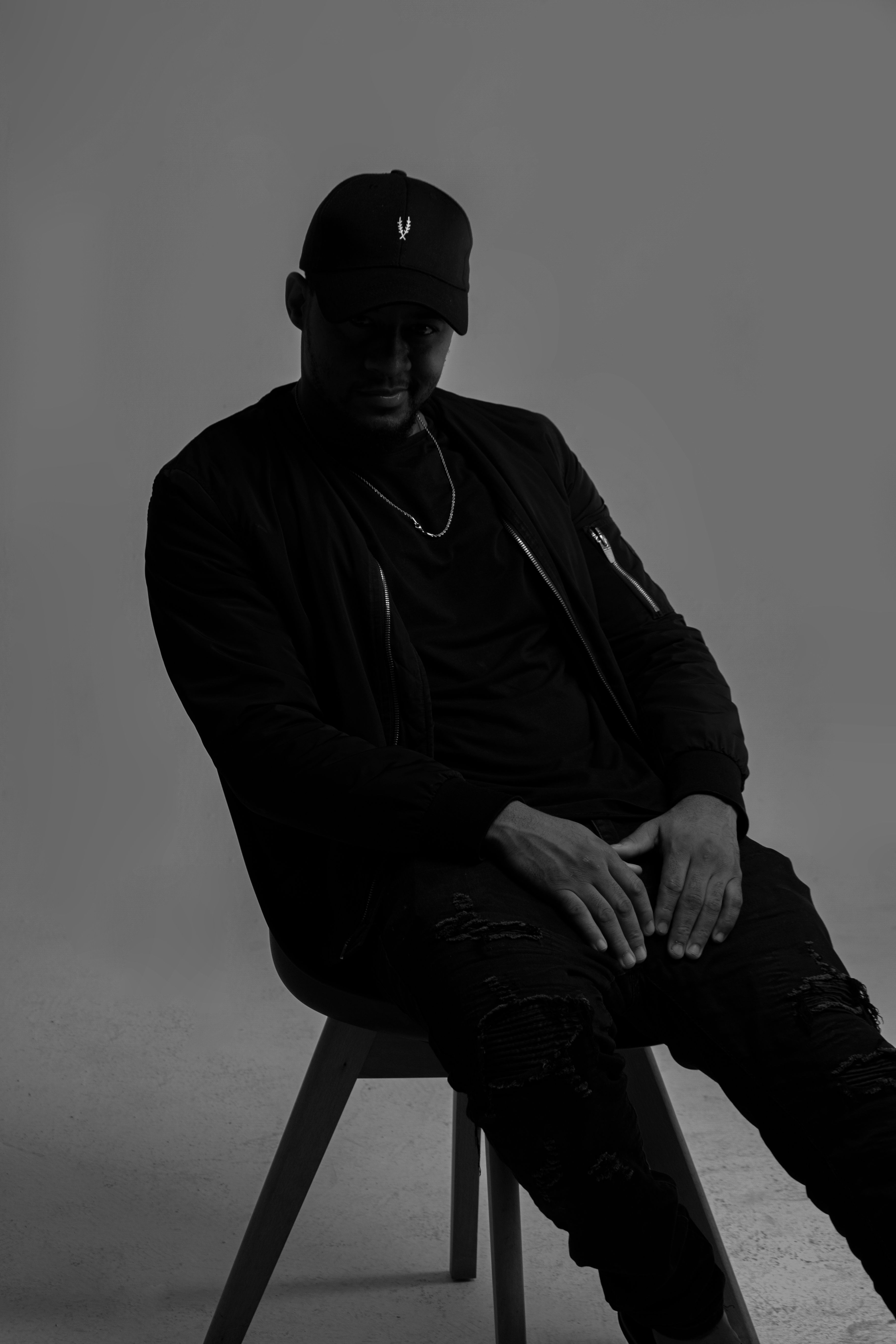 Black and white portrait of a man sitting in a studio, wearing casual attire.