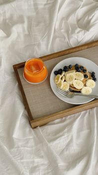 Delicious breakfast tray featuring pancakes with banana slices and blueberries, accompanied by fresh juice.