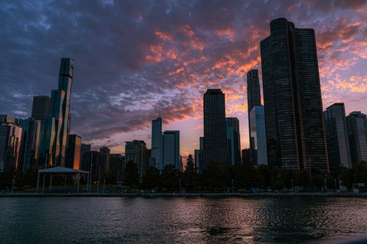 A stunning cityscape silhouetted against a vibrant twilight sky with colorful clouds reflecting on the water.