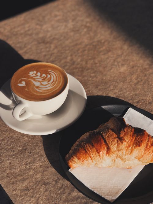Free Morning coffee with latte art and a croissant in a cozy café setting. Stock Photo