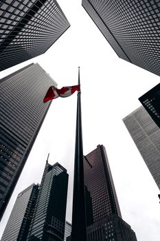 Low angle view of Canadian flag surrounded by skyscrapers in a bustling urban setting.