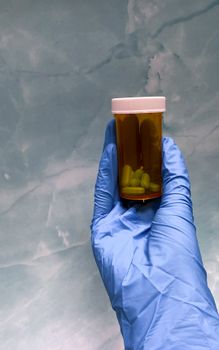 Close-up of a gloved hand holding a prescription pill bottle against a textured background.