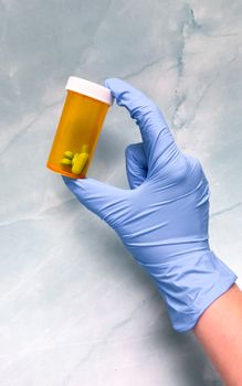 A gloved hand holding a prescription pill bottle against a textured background.