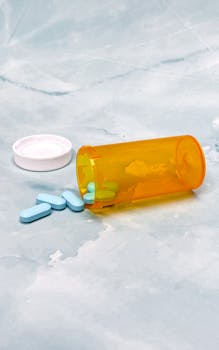 An overturned prescription pill bottle with blue tablets on a marble surface.