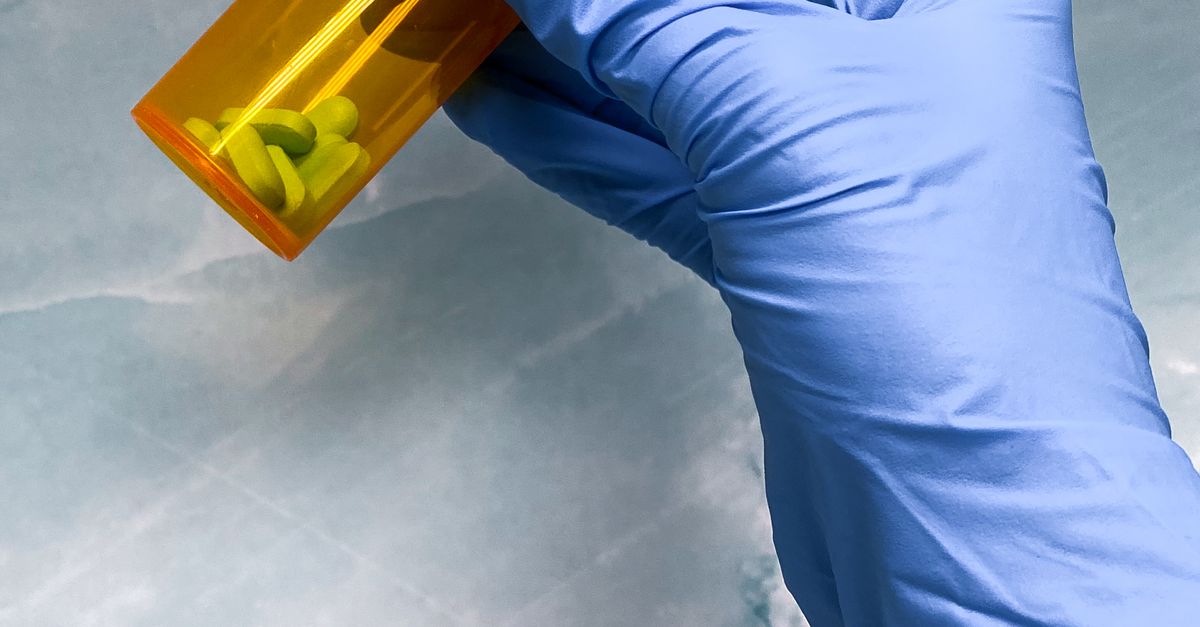 Hand in glove holding vial with pills