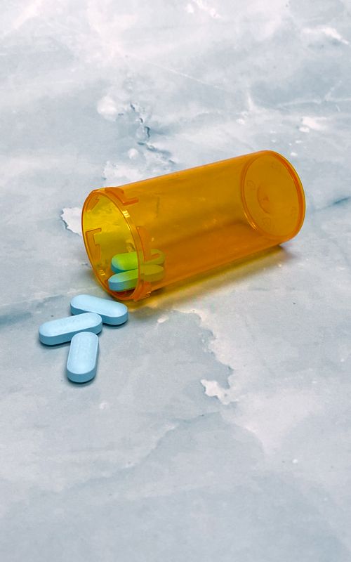 Free An orange pill bottle spilled, displaying blue tablets on a smooth marble surface, emphasizing healthcare and medication themes. Stock Photo