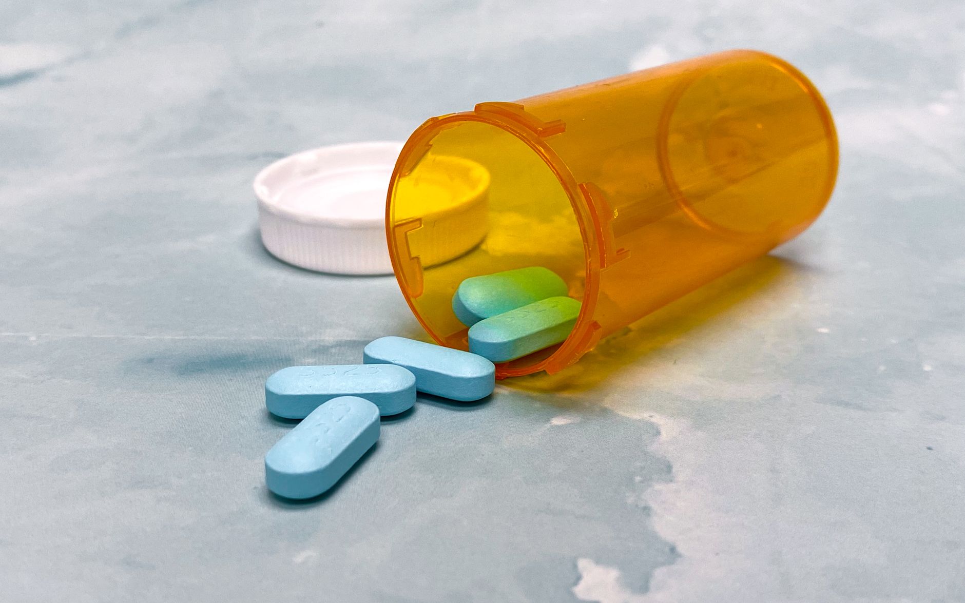 Blue pills spill from an orange vial on a gray surface, emphasizing healthcare themes.