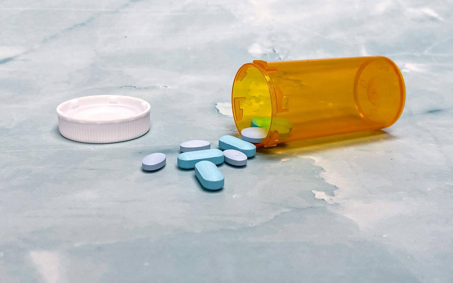 Scattered blue pills and an orange prescription bottle on a light surface.