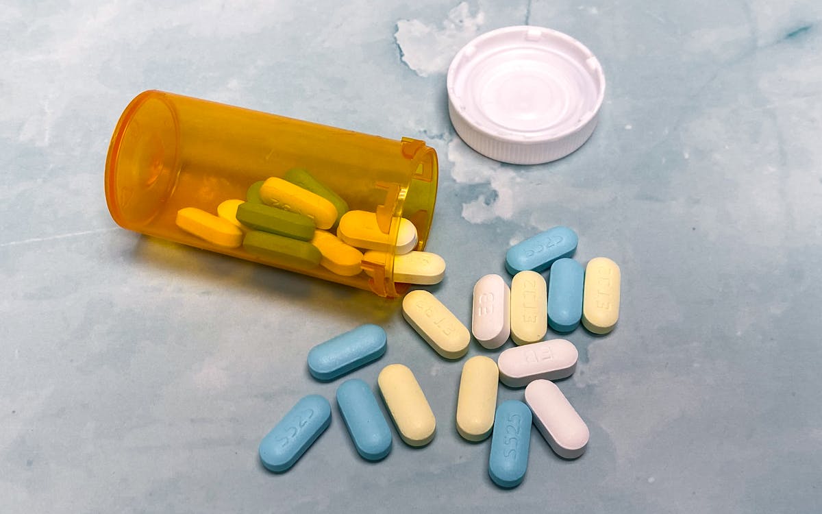 Free An open prescription bottle with assorted pills on a light blue background, high angle view. Stock Photo