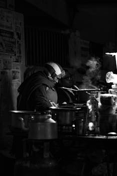 Elderly woman cooking at a street stall in Rishikesh, India, at night.