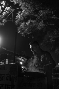 Black and white image of a street food vendor cooking at night in Rishikesh, India, emitting steam.