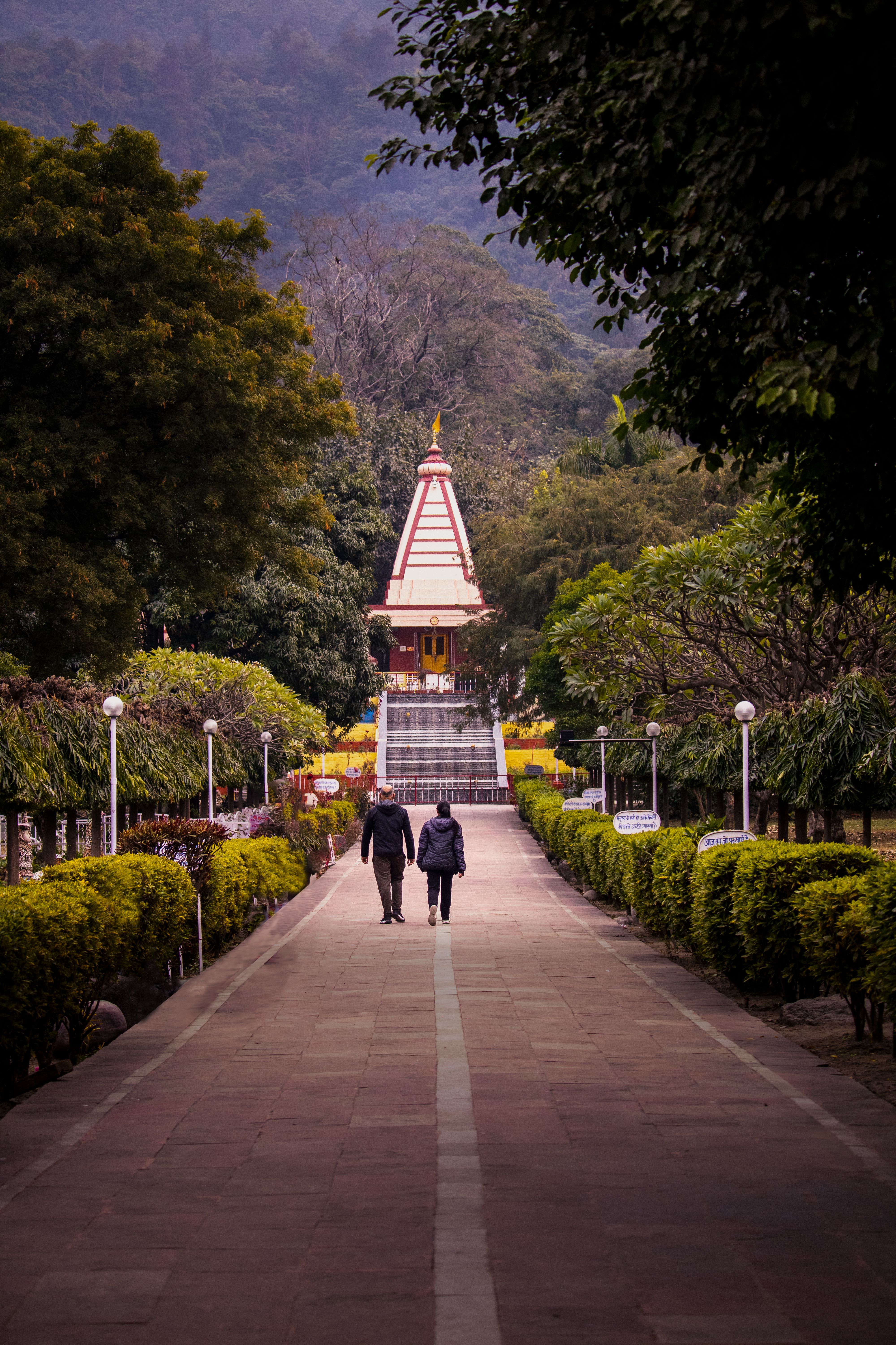 Serene scene of a couple walking towards a temple in a lush park setting in Rishikesh, India.