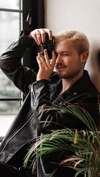 Stylish young man in a leather jacket taking a photo indoors.