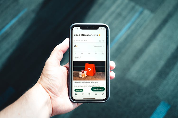 Photo Of A Hand Holding A Phone With A Delivery App On Screen