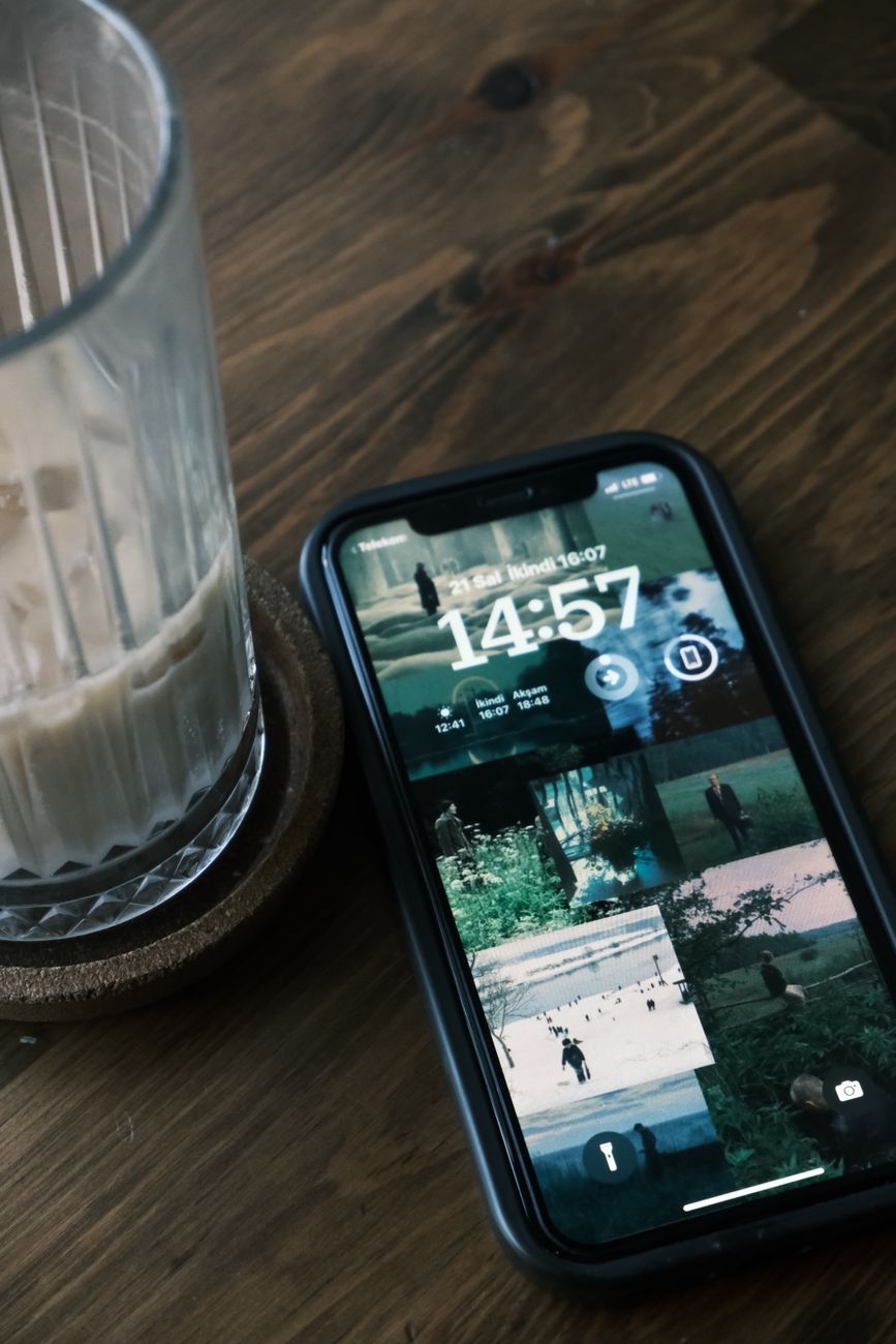 Close-up of a smartphone and a glass on a wooden table, displaying the time 14:57.