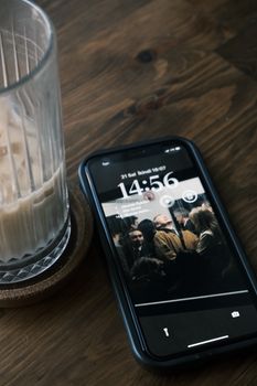 A glass of iced coffee and a smartphone placed on a wooden table, captured in a cozy indoor setting.