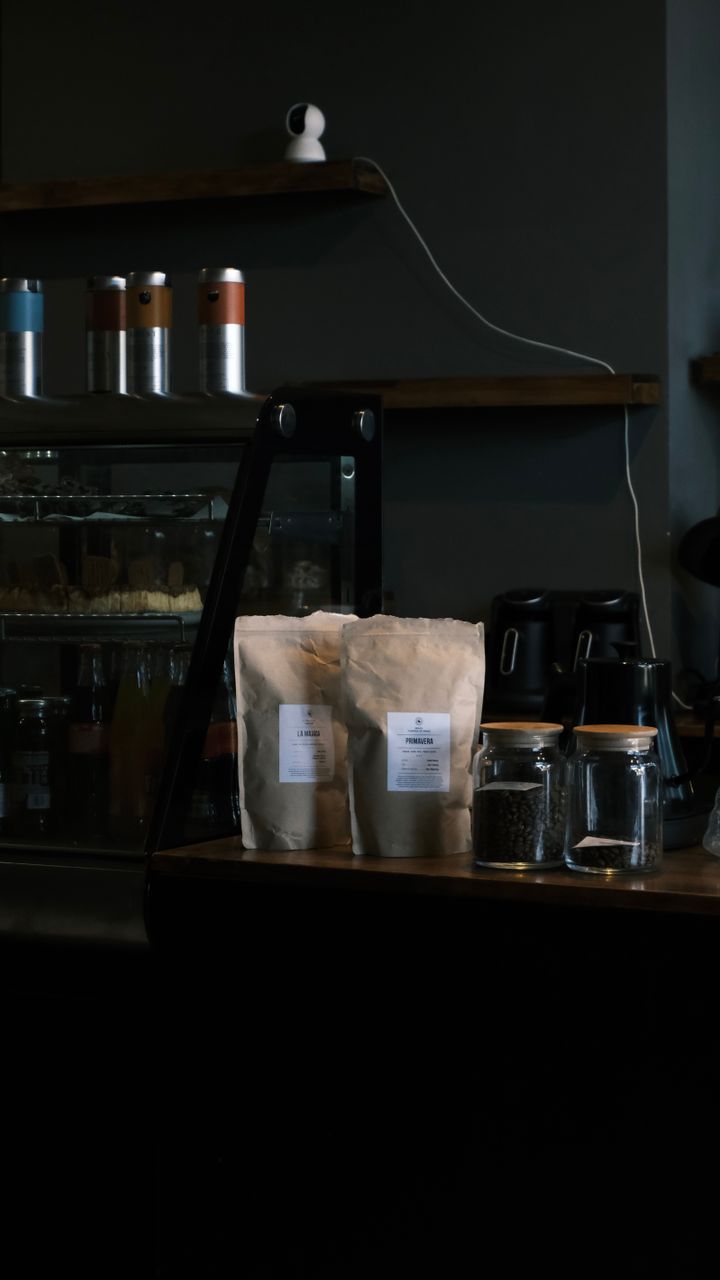 Clear glass storage jars holding coffee beans and loose leaf tea on a coffee and tea bar shelf