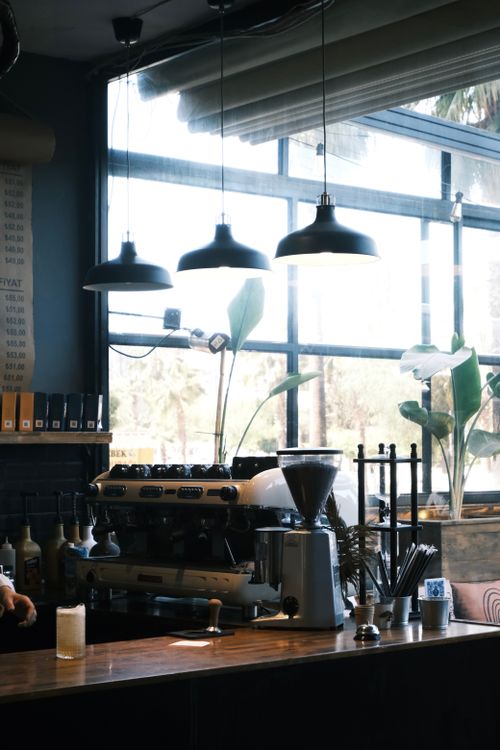 Free Stylish café interior featuring coffee machines and plants by large windows with pendant lighting. Stock Photo