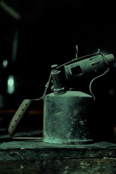 Old rusty blowtorch on a wooden table in a dimly lit workshop setting.