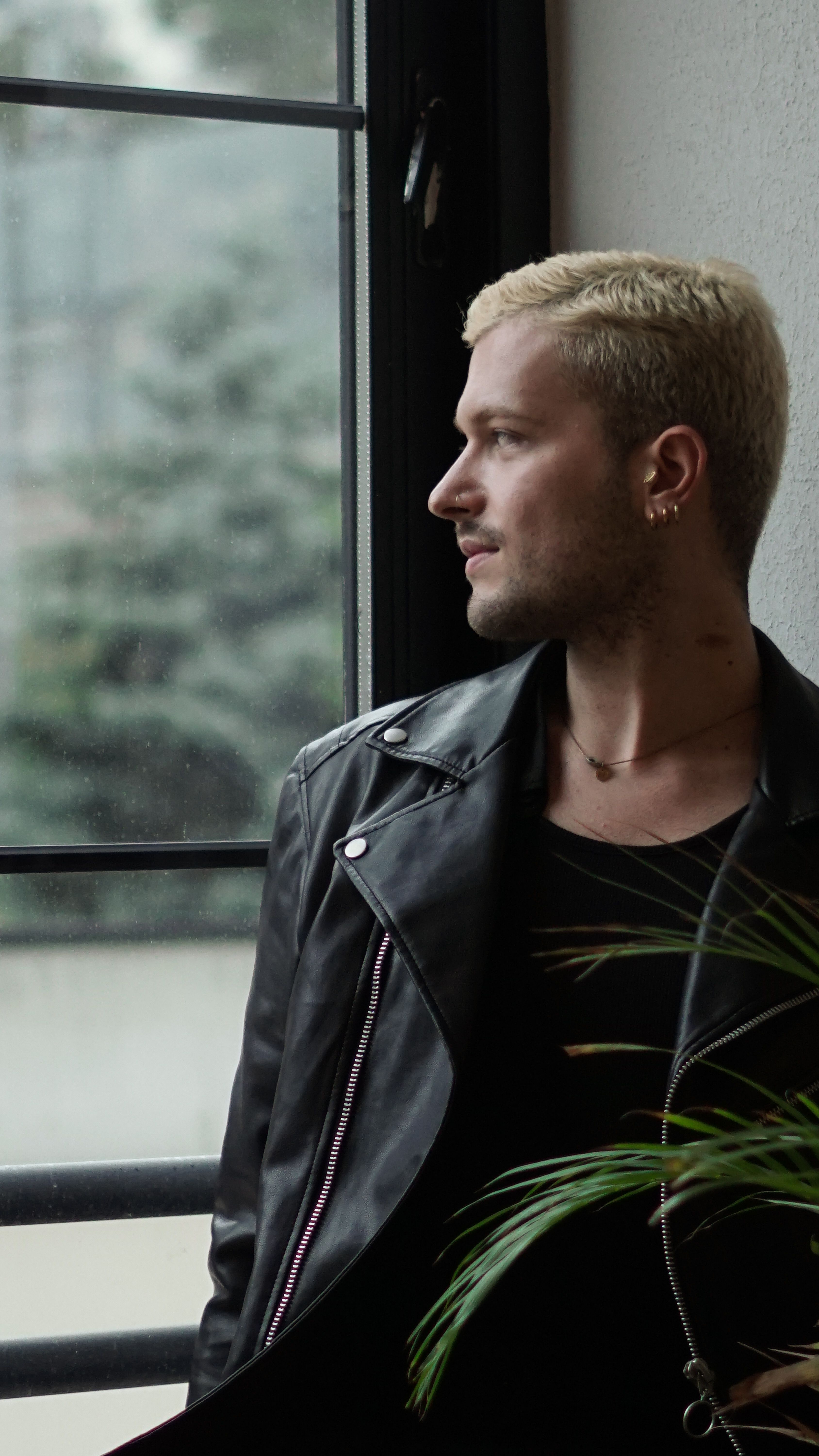 Pensive man in leather jacket gazing outside, creating a moody indoor scene in Istanbul.