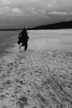 A man walks along a deserted beach in a black and white landscape.